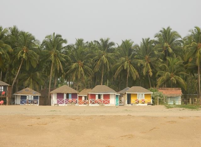 A row of brightly painted wooden beach huts under coconut palms at Agonda beach