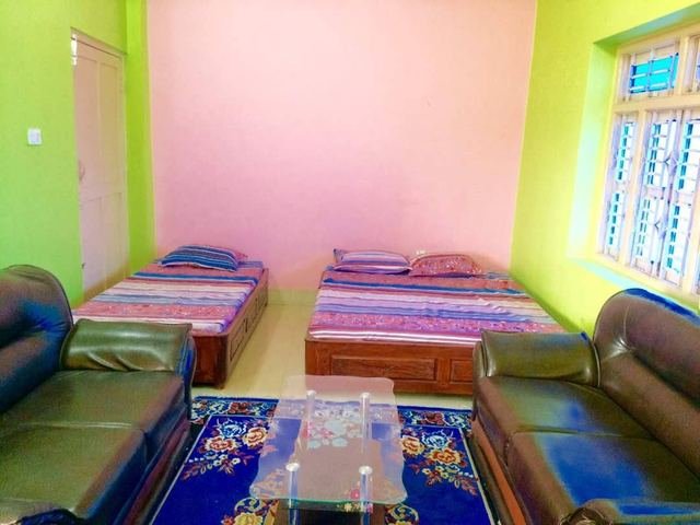 A larger room with pink and green walls, two beds, two leather sofas, a glass coffee table and a patterned rug