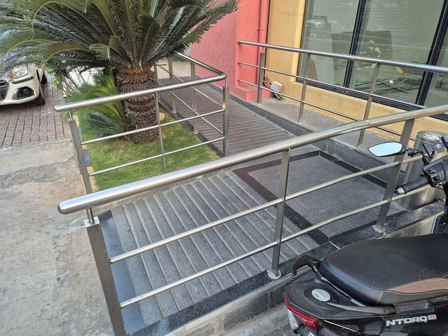A sloped ramp with steel handrails leading to a hotel entrance, beside a small garden