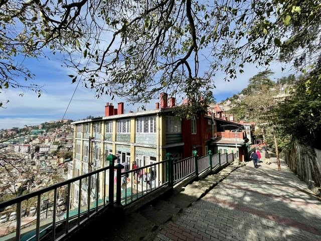 A stepped paved path with railings running downhill beside buildings on the Mall Road area of Shimla, with the hillside town behind